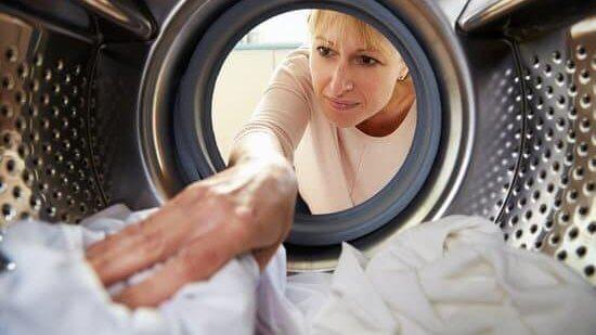Nainen ottaa pyykkiä pois pyykinpeukoneesta.