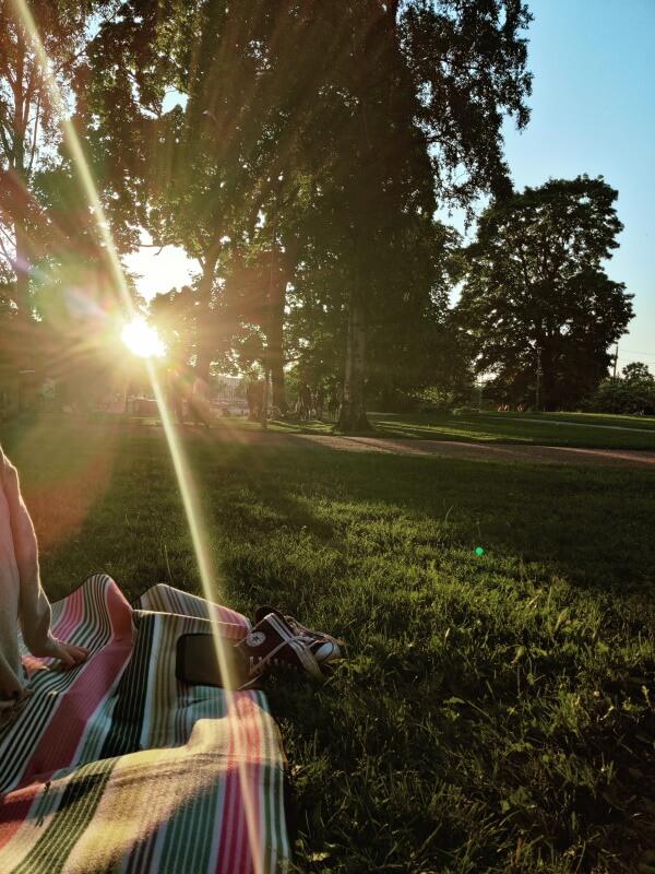 Kuvassa piknikviltti puistossa ja laskeva aurinko.